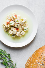 Top view of marinated feta cheese cubes on white plate. Cheese cubes marinating in herbed oil, flat lay of feta cheese in olive oil on plate