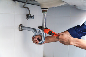 Plumber working in the bathroom, plumbing repair service, repairing leaking sinks with adjustable wrench, assemble and install concept.