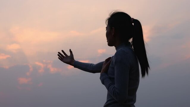 Silhouette of a woman with her arms raised in worship to God.Catholic Easter. concept of christianity Struggle and victory for God. Praise God spiritually and religiously.4K slow motion.