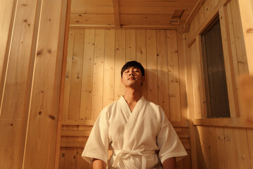 Relaxation Asian man in bathrobe sitting relaxing in the sauna. Young man healthcare and spa...