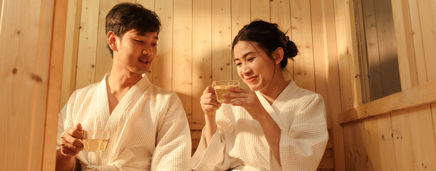 Relaxation Asian couple in bathrobe drinking hot tea and having cheerful conversation while...