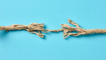 Tension, separation, danger or risk concepts. Frayed rope is about to brake on blue background with copy space.