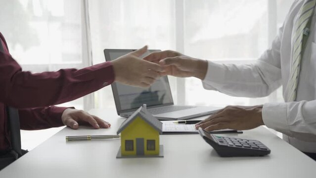 Real estate agent shaking hands with male client agreeing to sign house for sale after businessman shows model of mortgage home building project 4k