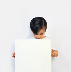 boy with head down, looking at a white piece of paper held in his hands wearing a white T-shirt on...