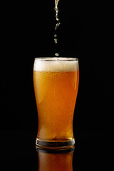Pouring beer into a glass on a black reflective background.
