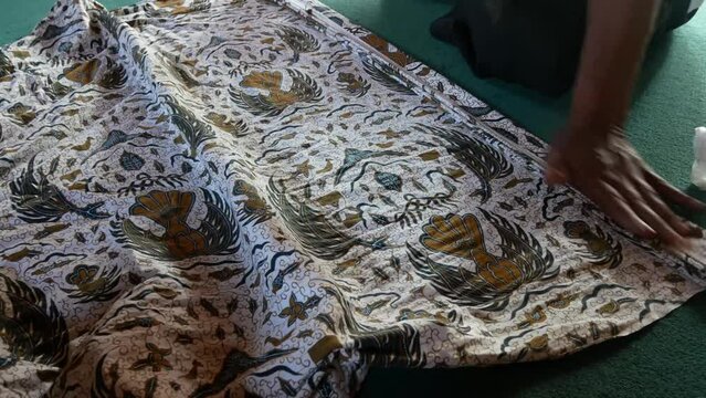 a person is tidying up a traditional Javanese jarik batik cloth to wear (wiru)