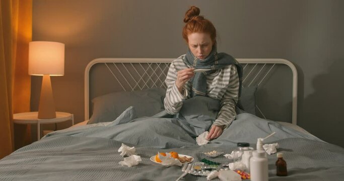 red-haired sick, flu-ridden young woman has problems with health, scared shocked girl has high headache, she has fever, flu and check mometer, measure body temperature, Slow motion self-isolation