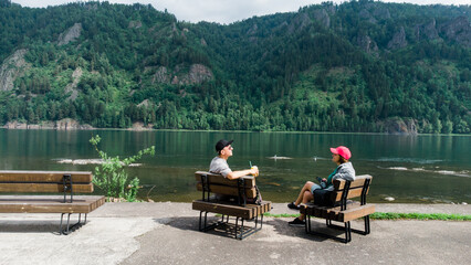 man and woman sit back in bench enjoying valley landscape view. adult tourists couple, sitting in the bench. Panoramic view of mountain hills and river