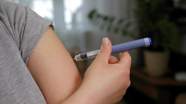 Close-up of a young woman injecting insulin into her arm with an insulin pen. Treatment of diabetes. 