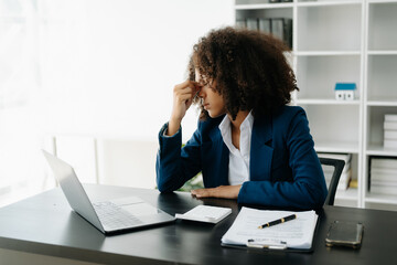 Overworked young African businesswoman office worker suffering from neck pain after had a long day at her office table. office syndrome concept