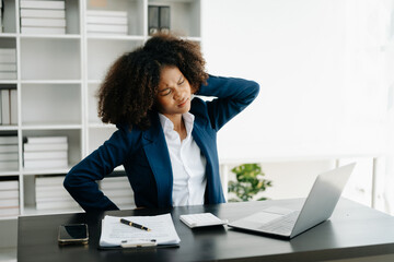 Overworked young African businesswoman office worker suffering from neck pain after had a long day at her office table. office syndrome concept