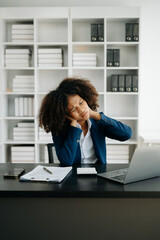 Overworked young African businesswoman office worker suffering from neck pain after had a long day at her office table. office syndrome concept