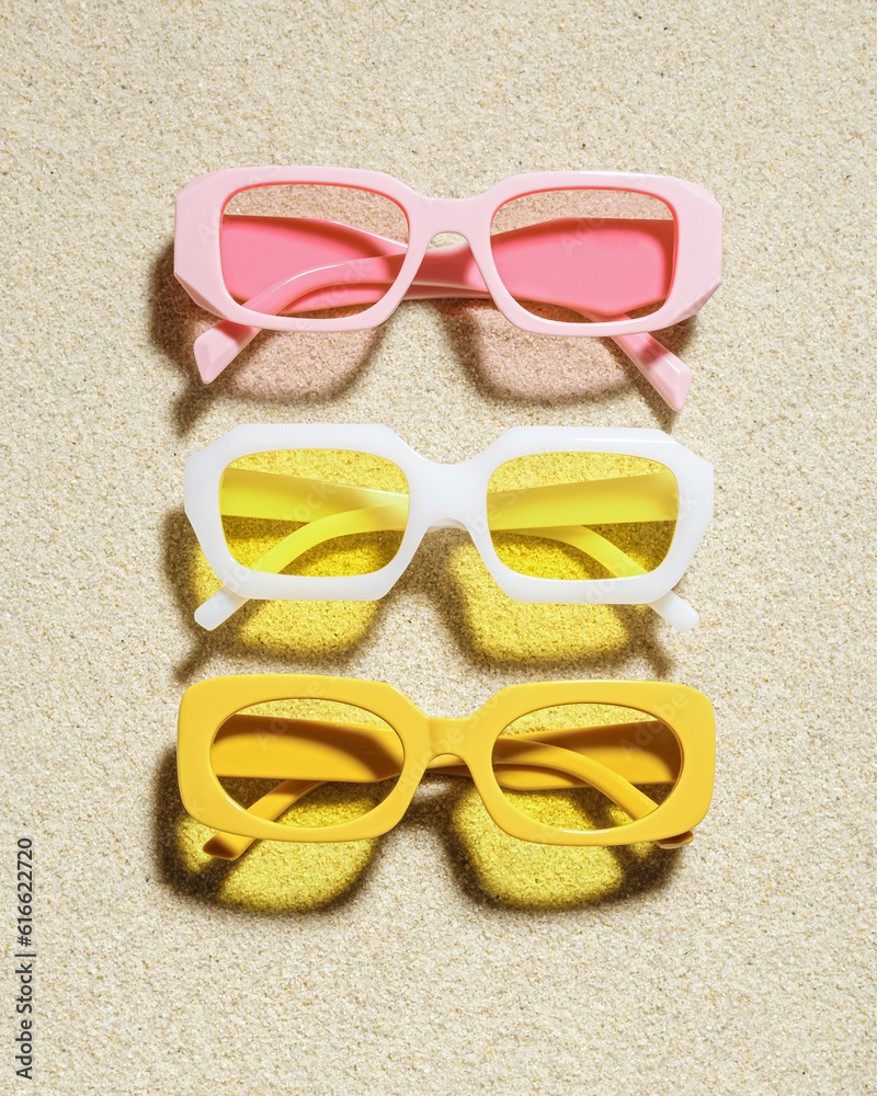 Poster stylish colored sunglasses on sand background at sunlight, summer fashion collection eyeglasses with