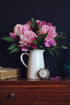 Bouquet of pink peonies on a dark background. Garden summer flowers, a clock and a book.
