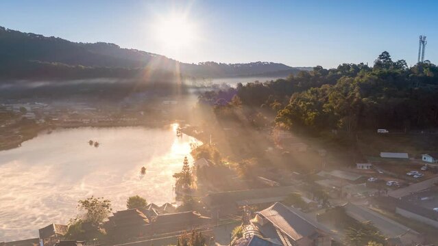 Drone view with fly above lake at Baan Rak Thai village in Mae Hong Son, Thailand and go to sunrise over mountain or hill with fog or mist covering village.