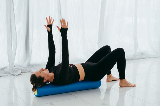 Fitness trainer woman in black fitness clothes in the training room flexes with a massage roll on floor in pilates class. 