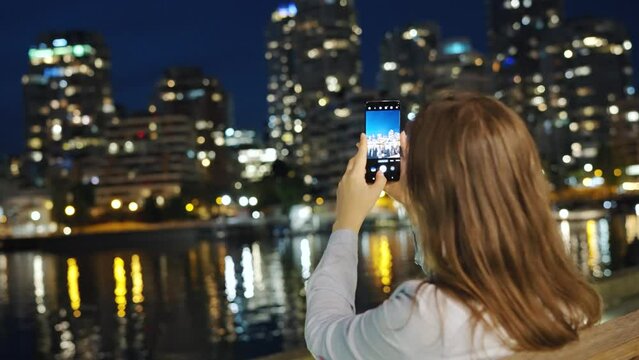 Woman takes pictures of the skyscrapers of Vancouver on her smartphone at night