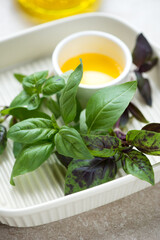 Closeup of fresh green basil leaves and olive oil in a beige serving tray, vertical shot, selective focus
