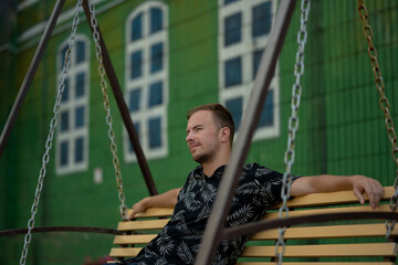 a young adult man sits on a swing, has a rest and looks up at the sky