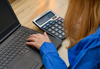 Kobieta przy biurku używająca kalkulatora i laptopa  - obrazy, fototapety, plakaty