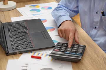 Mężczyzna pracujący przy biurku, liczący na kalkulatorze  - obrazy, fototapety, plakaty