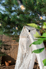 A white net canopy with a chandelier and cushions hangs from a pine tree in the garden