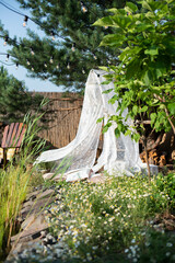 A white net canopy with a chandelier and cushions hangs from a pine tree in the garden