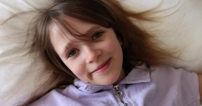 Smiling little girl takes selfie and falls on bed. Smiling cute child taking video portrait