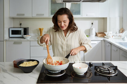 Smiling woman enjoying smell of frying vegetables when cooking spaghetti sauce for dinner