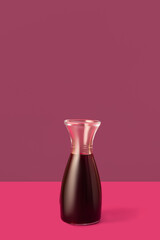 Decanter with red wine on pink background