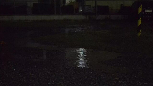 Puddle in a parking lot during a rainstorm. Raining on the ground. Dark parking lot during heavy rain. Raining in the city.