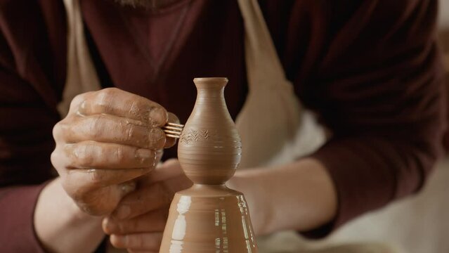 Potter adds unique lines to vase on potter's wheel. Close-up of potter's hands. Concept of craft and art. 4K, UHD