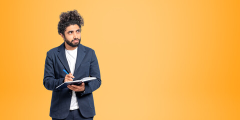 Thoughtful Arabic college student man portrait with notebook and pen, orange