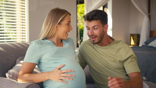 Couple with pregnant woman in bedroom at home with man feeling baby kicking - shot in slow motion