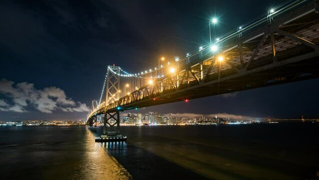 Lockdown Time Lapse Shot Of Illuminated Oakland Bay Bridge Over Sea Near City Against Sky At Night - San Francisco, California