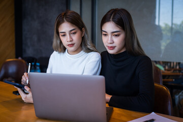 Two cheerful young Asian female college students working on the school project using laptop computers and tablets together in private study room