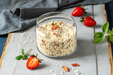 Risotto raw mix with strawberries and herbs in a glass container, fresh strawberries, sage, napkin over grey wooden and blue background