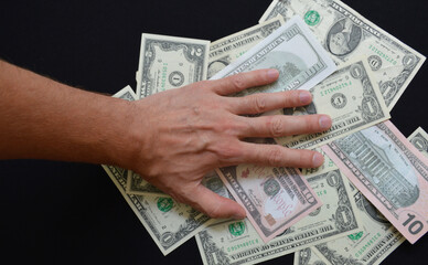 hand on chaotically scattered dollars on a black background. rejection of dollar settlements in...
