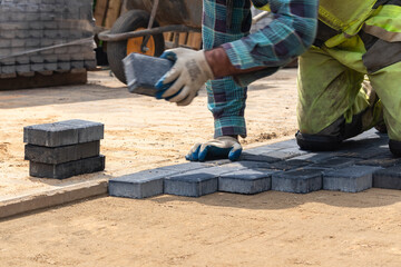 A worker laying paving stones at a sidewalk construction site, close up
Pracownik układający kostkę brukową na placu budowy chodnika, z bliska