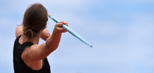 Female athlete throwing a javelin onto a grass field during a track and field campetition, rear view