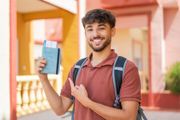 Young Arabian handsome man holding a passport at outdoors and pointing it