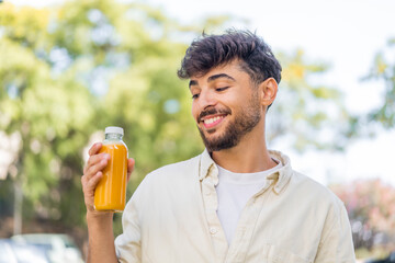 Fototapeta premium Young Arabian handsome man holding an orange juice at outdoors with happy expression