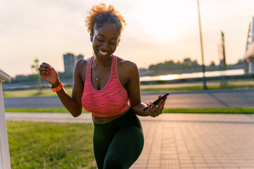 On the riverside pathway, the African American girl sets up her headphones, ready to indulge in her favorite music and kickstart her training session. - Powered by Adobe