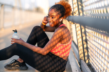 The athletic girl, dressed in sportswear, takes a seat on the pedestrian path of the bridge,...