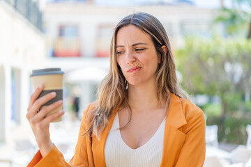 Young pretty woman holding a take away coffee at outdoors with sad expression