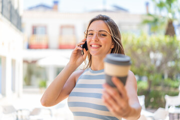 Young pretty woman at outdoors using mobile phone and holding a coffee with happy expression