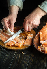 The cook cuts a fresh trout fish carcass. Chef hands with a knife while cleaning red fish. The idea of a fish diet