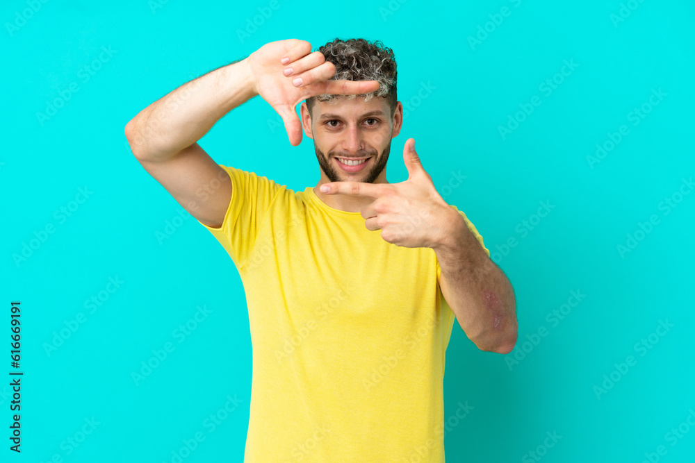 Wall mural Young handsome caucasian man isolated on blue background focusing face. Framing symbol