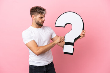 Young handsome caucasian man isolated on pink background holding a question mark icon