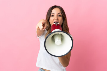 Young Romanian woman isolated on pink background shouting through a megaphone to announce something...